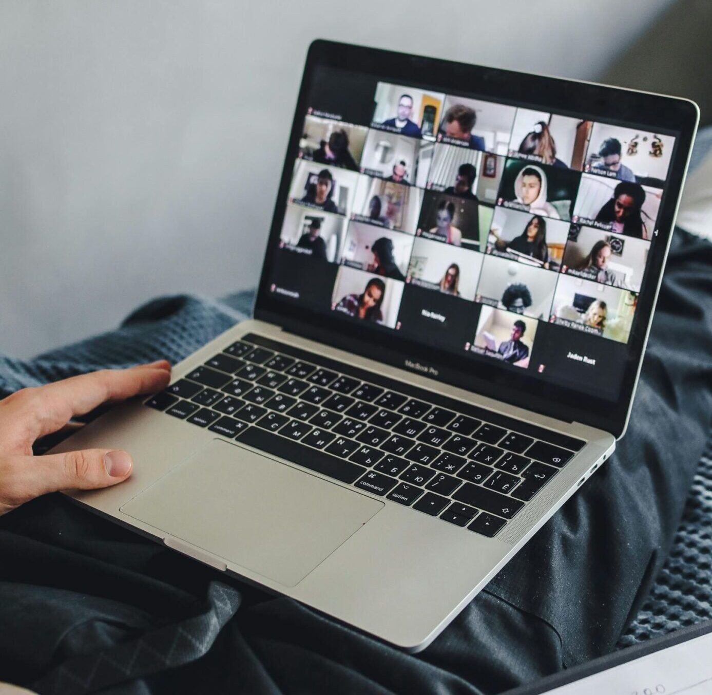 Adult sitting on bed using laptop for video conference and note-taking.
